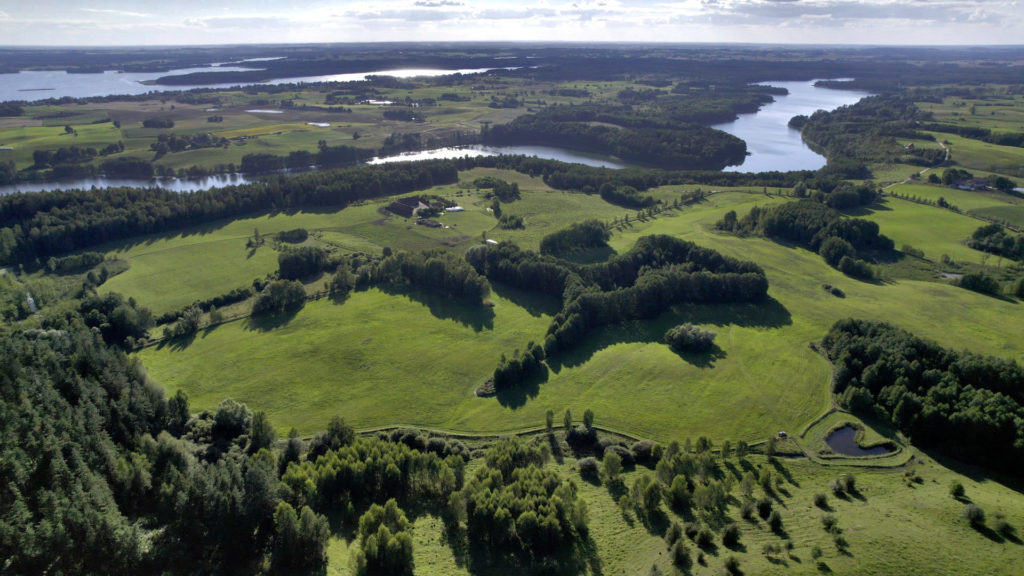 Widok z lotu ptaka. Zielony, pagórkowaty teren zlokalizowany nad jeziorem. 50 hektarów na sprzedaż