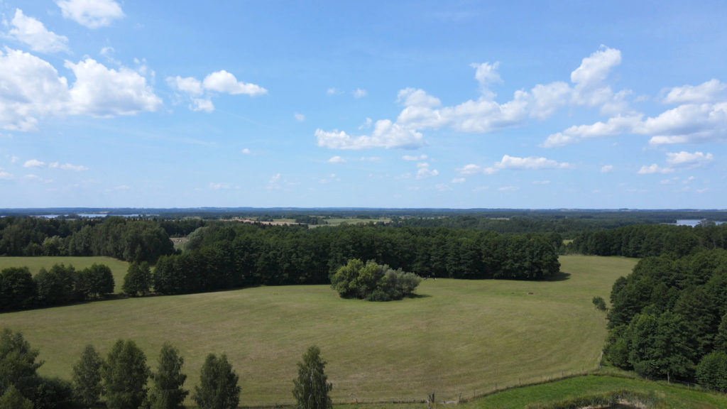 Widok z lotu ptaka. Zielony, pagórkowaty teren zlokalizowany nad jeziorem. 50 hektarów na sprzedaż